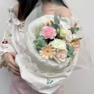 A woman holding a pastel pink and white flower bouquet, wrapped in sheer white paper with a ruffled edge.