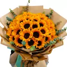 A large bouquet of sunflowers wrapped in brown paper with eucalyptus leaves.