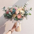 Bouquet of pink, yellow, and cream roses with eucalyptus in a wooden vase tied with a white ribbon.