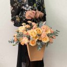 Peach roses, gerbera daisies, and carnations in a kraft paper flower basket.