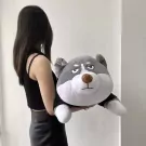 A woman holds a large, grumpy-faced husky plush toy.