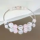 A bracelet with pink and clear beads and silver charms on a white fabric.
