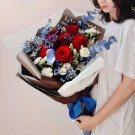 A bouquet of red roses with blue and white accent flowers and eucalyptus leaves, tied with a blue ribbon.