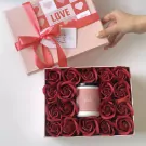 Gift box with red roses and a candle, tied with a pink ribbon.