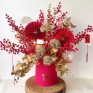 Red and gold floral arrangement with a lucky cat, red berries, fans, and orchids in a pink box.
