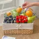 A fruit basket filled with oranges, pears, strawberries, and grapes, decorated with small white flowers.