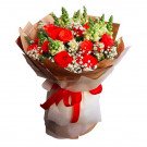 Vibrant bouquet of red roses, green snapdragons, and baby's breath, wrapped in brown paper and tied with a red ribbon.