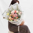 A bouquet of pink and white roses and other flowers wrapped in newspaper.