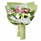 Pink lotus flowers, lotus seed pods, white carnations, and yellow flowers in a green bouquet wrap.