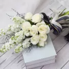 White roses and stock flowers bouquet on a stack of light blue books with a dark ribbon.
