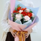 Buket bunga mawar krim dan gerbera oranye cerah dibungkus kertas merah muda dan biru pastel dengan pita emas.