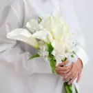 Bride holding a white bouquet of calla lilies and alstroemeria with lace.