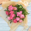 Bouquet of pink lotus flowers with green leaves and ferns, wrapped in sheer gold fabric.