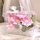 Pink lotus flowers in a clear square box with a white ribbon.