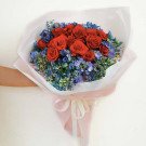 Bouquet of red roses and blue hydrangeas with white and pink wrapping, tied with a ribbon.