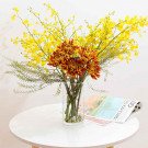Yellow orchids and orange chrysanthemums in a glass vase on a white table.