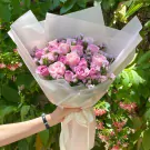 Pink and lavender roses in a bouquet wrapped in sheer paper, held by a hand with a black watch.