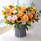 Boxed arrangement of sunflowers, pink and orange roses, and baby's breath in a grey box.