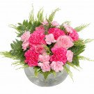 Round glass vase with pink carnations, roses, and ferns.
