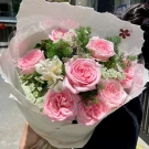 Bouquet of pink roses, white filler flowers, and greenery wrapped in white paper.