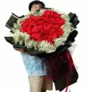 A person hugging a large bouquet of 101 red roses with baby's breath.