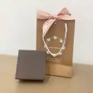 A brown gift box and a shopping bag with a pink bow, containing a bracelet with diamond-like stones.