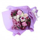 Bouquet of pink and white carnations, roses, and chrysanthemums in purple paper with a white ribbon.
