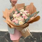 A woman holds a large bouquet of pink and white roses wrapped in brown paper.