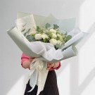 A person holding a pale green bouquet of white chrysanthemums and carnations, tied with a ribbon.