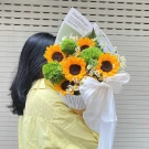 A bouquet of sunflowers and green filler flowers wrapped in newspaper with a white ribbon.