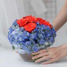 Red roses and blue hydrangeas in a glass vase, held by hands.