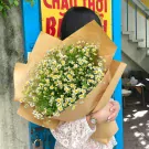 Woman holding a bouquet of small white and yellow daisies wrapped in brown paper.