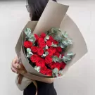 A bouquet of red roses and eucalyptus, wrapped in brown paper with a ribbon.