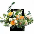 Black basket with orange and pink roses, white carnations, and eucalyptus.