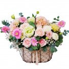Pastel pink and cream flower arrangement in a wire basket with lace ribbon.