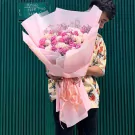 A man holding a large bouquet of pink and white roses wrapped in pale pink paper.