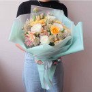 A pastel bouquet of roses, narcissus, and scabiosa in light green wrapping.