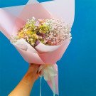 A hand holding a pink-wrapped bouquet of hydrangeas and baby's breath.