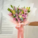 A pink lily and mixed flower bouquet wrapped in white paper with a pink ribbon.