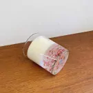 A clear glass candle with white wax and pink petals embedded in the bottom half.