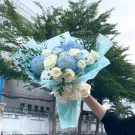 Bouquet of blue chrysanthemums, white roses, and greenery tied with a cream bow.