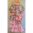 A pink tiered floral arrangement with roses, orchids, and other flowers on a stand with a congratulatory banner.