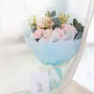 Bouquet of pink roses, chamomile, and eucalyptus leaves wrapped in pale blue paper with a white ribbon and card.