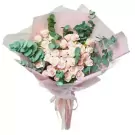 Bouquet of light pink roses and eucalyptus leaves, wrapped in pink paper.
