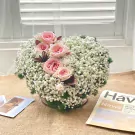 Heart-shaped arrangement of pink roses and baby's breath on a burlap surface.