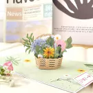 Pop-up card with a 3D basket of colorful flowers and a newspaper in the background.