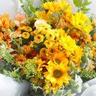A bright bouquet of yellow and orange flowers, including sunflowers, chrysanthemums, and carnations.