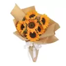 Bouquet of six sunflowers wrapped in brown paper and tied with a white ribbon.