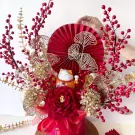 Maneki-neko cat with red fan, berries, and gold leaves in a red flower box.