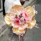 A bouquet of pink and cream flowers in a layered light pink and cream wrapper, tied with ribbons.